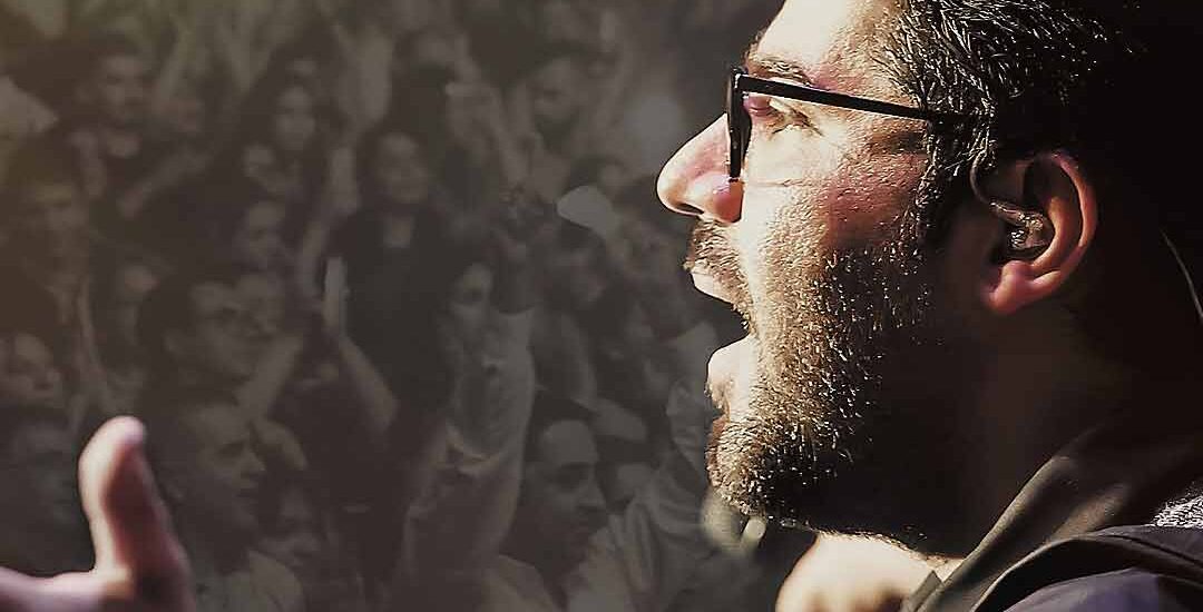 Hamed Homayoun passionately performing on stage in Australia with a cheering crowd in the background, captured by HAPfilm, the best events international videographer in Auckland.