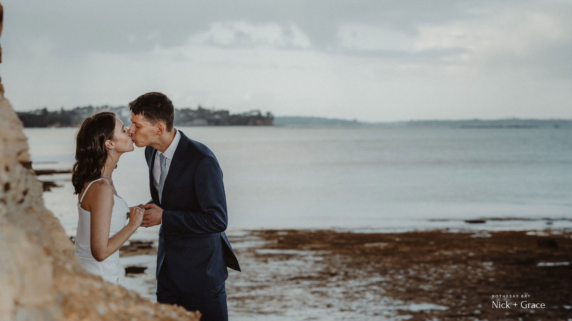 Auckland backyard wedding captured by HAPfilm featuring the couple sharing their first kiss by the beach.