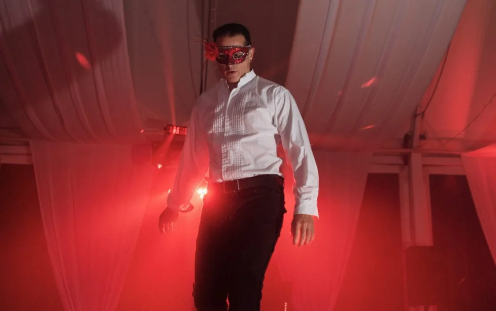 Three masked performers from the Men of Steel on stage at Allely Estate, illuminated by red lights, engaging in a playful and naughty act.