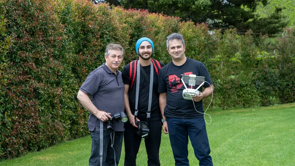 Three HAPfilm crew members holding a drone and cameras in the yard at Allely Estate, ready to capture wedding moments.