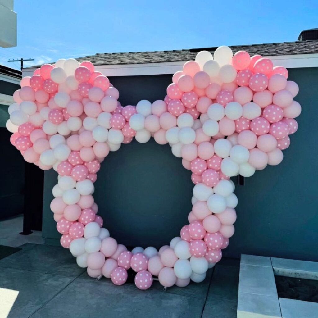 Large pink and white Minnie Mouse-shaped balloon frame with polka dots, designed for a themed birthday party photo booth in Auckland