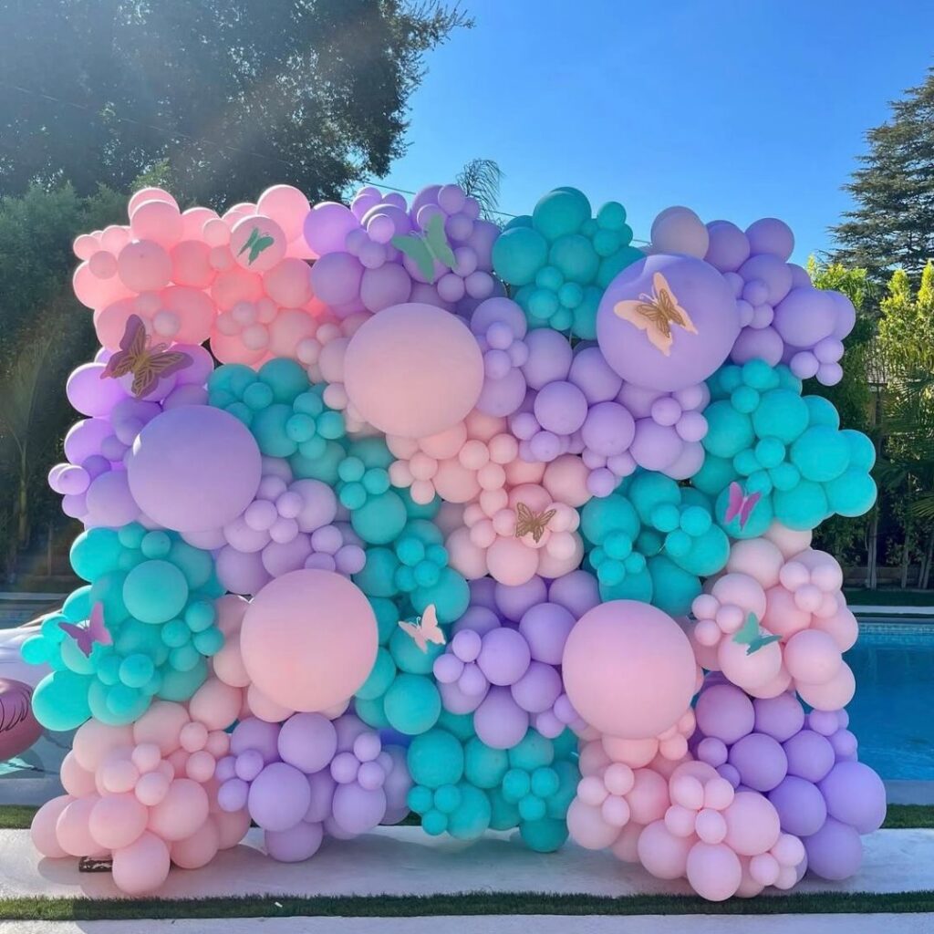 Large organic balloon wall backdrop in pastel pink, purple, and teal, decorated with gold butterflies, ideal for a spring or fairy-themed party in Auckland.
