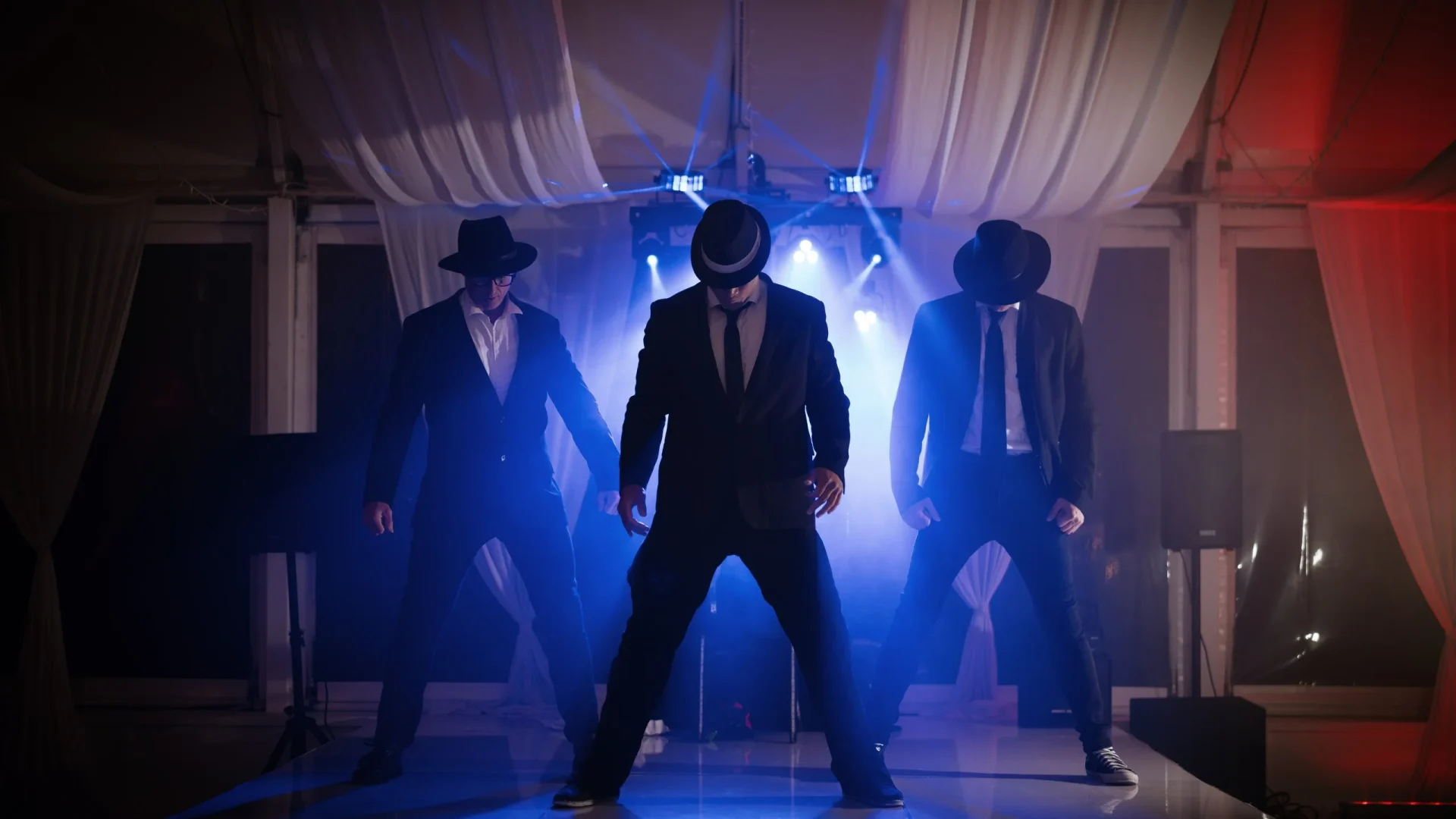 Three performers from the Men of Steel dressed in suits and hats, standing on stage with dramatic lighting at Allely Estate.